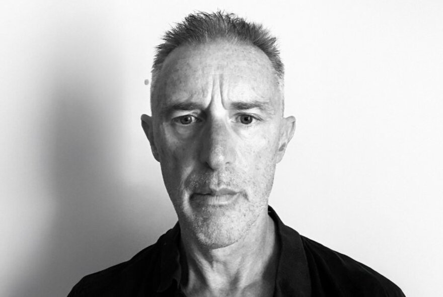 Black and white portrait of sports journalist and cricket commentator, Gideon Haigh, looking directly at the camera with a blank expression.