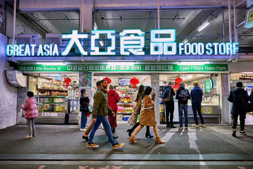 A group of friends walking past a brightly lit grocery store at night.