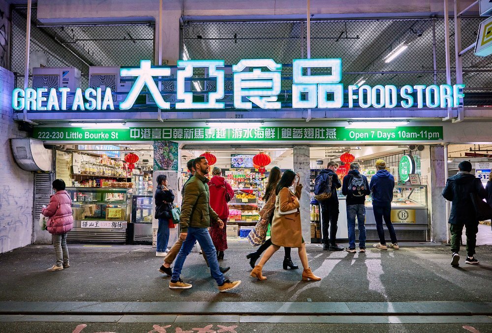 A group of friends walking past a brightly lit grocery store at night.