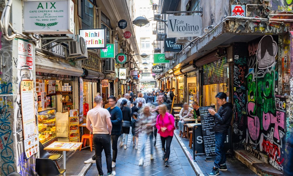 A busy laneway with cafes covered in graffiti.
