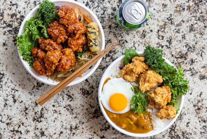 Looking down on a table at two bowls on fried chicken, on with curry, rice and and an egg.