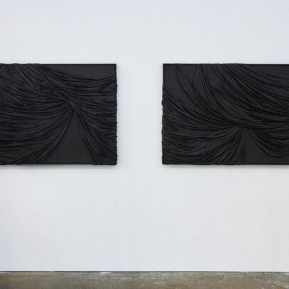 Two dark contemporary artworks on a white wall in a gallery.