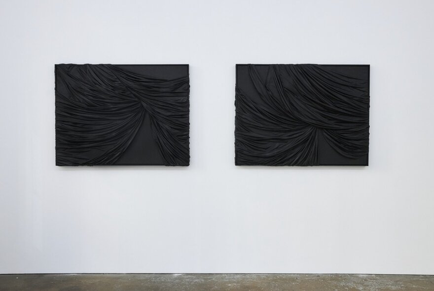 Two dark contemporary artworks on a white wall in a gallery.