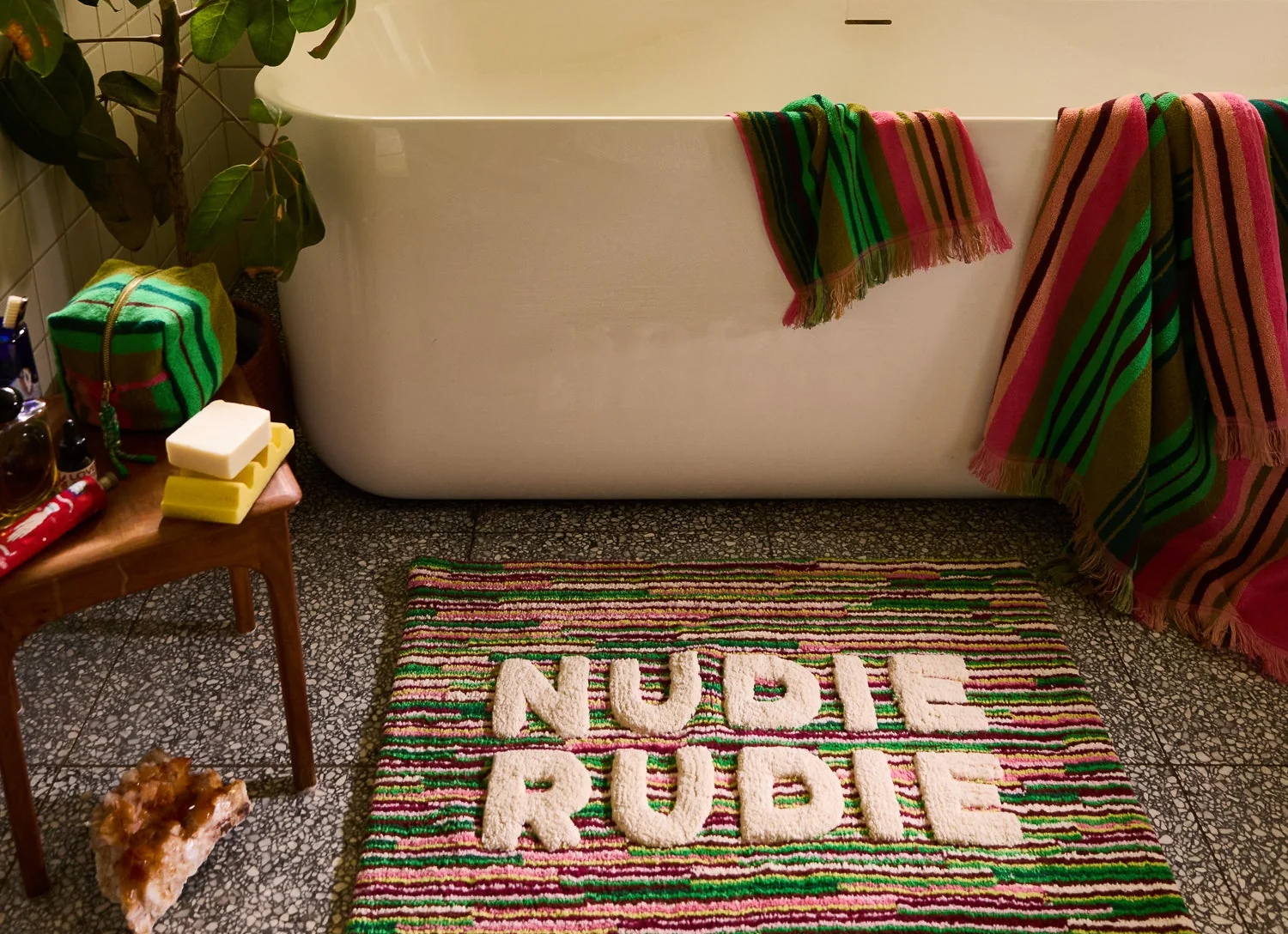 A bath with a mat that reads 'nudie rudie'.