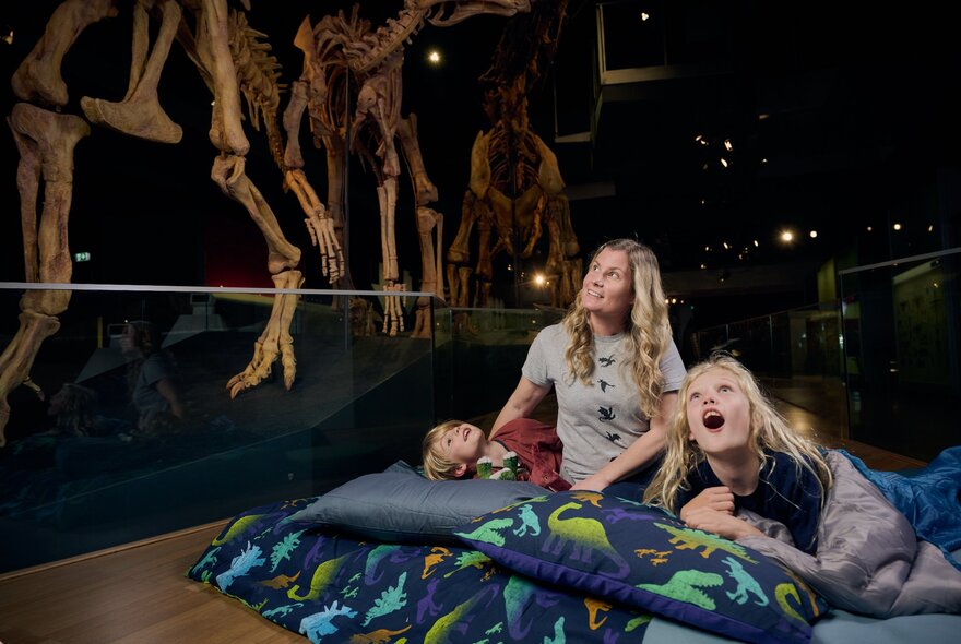 Mother and children lying in sleeping bags surrounded by dinosaur skeletons.