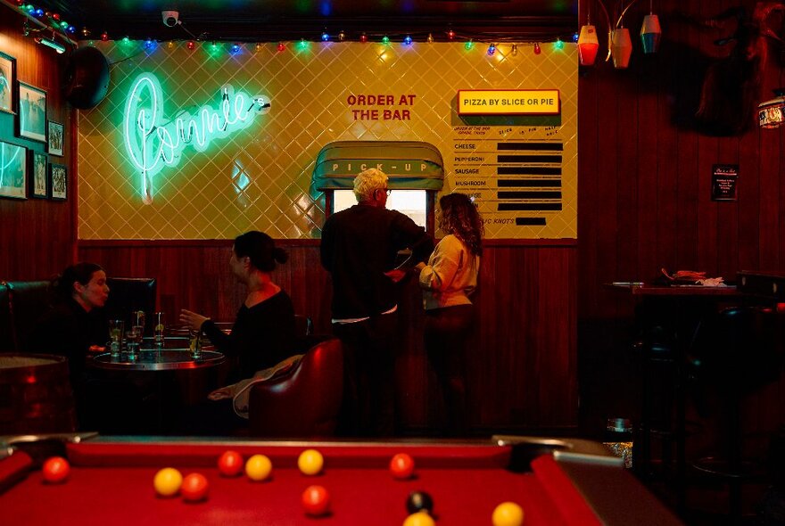 People mingling in a bar with a pool table and green neon light. 