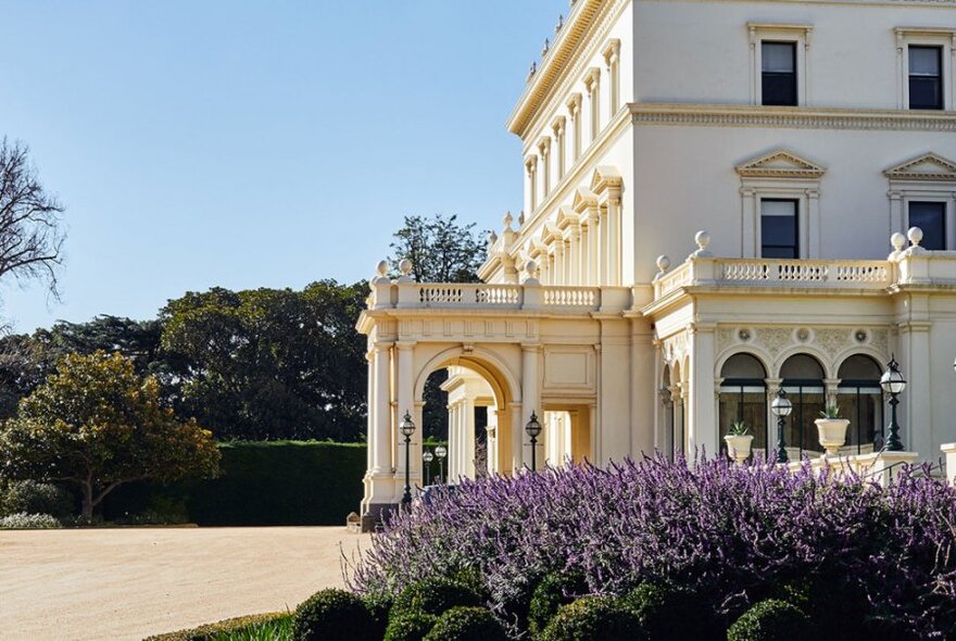 Exterior of white stucco Government House with arched portico and gabled windows.