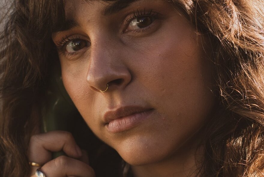 Close up of a woman's face, she has a nose piercing, brown eyes and has a neutral expression.