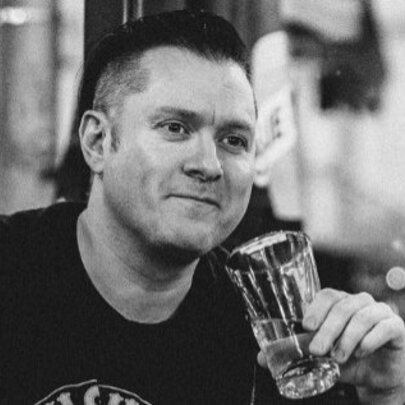 Black and white photograph of the founder of the Tough Guy Bookish Club, Shay Leighton, drinking a beer and smiling slightly.