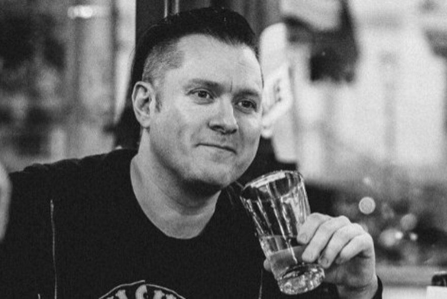 Black and white photograph of the founder of the Tough Guy Bookish Club, Shay Leighton, drinking a beer and smiling slightly.