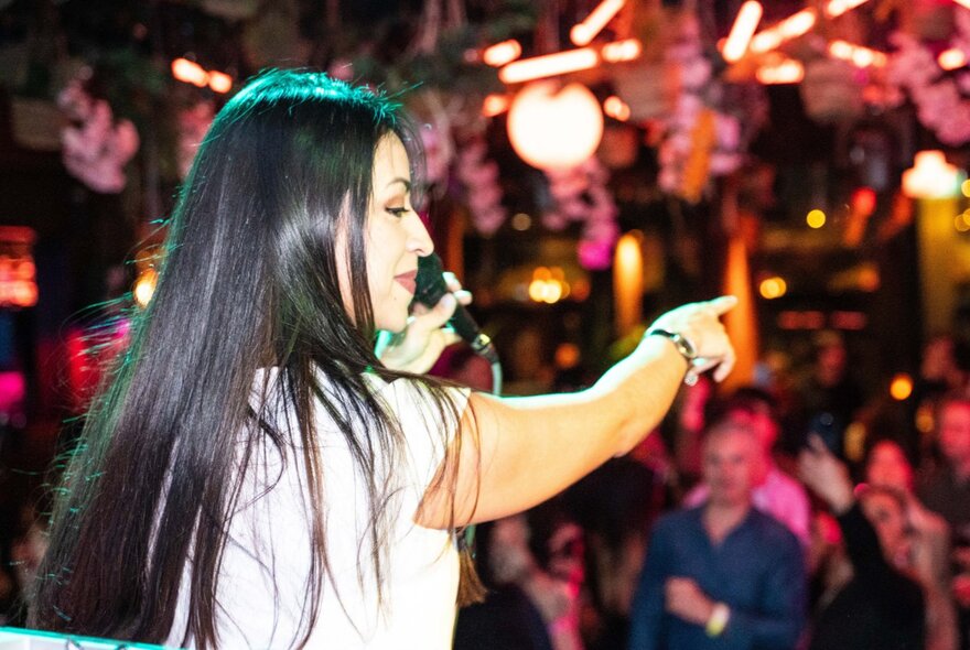 A woman on stage holding a microphone as if about to sing, playing to a crowd of people on a dance floor.