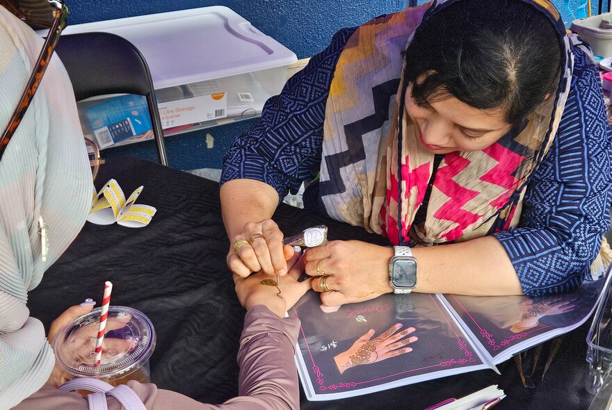 A woman decorating another woman's hand with henna. 