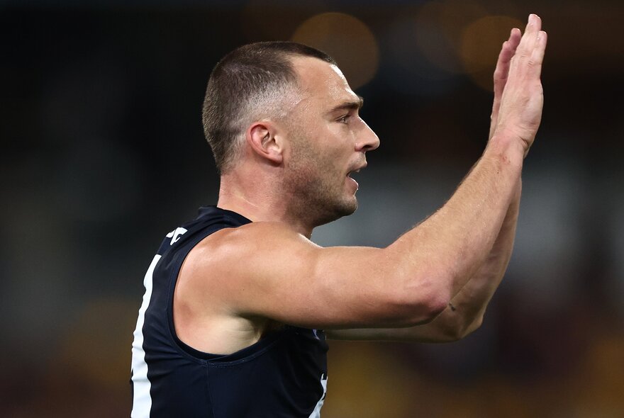 A Carlton AFL player with his arms raised with open palms as if about to high five somebody who is not in the image.