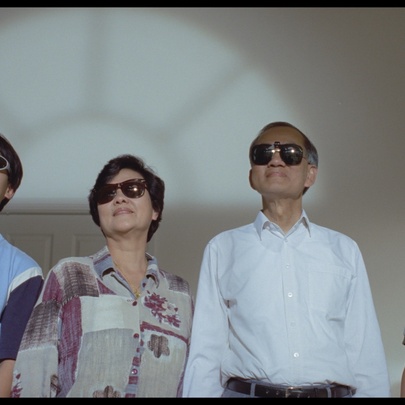 A still from the film Floating Life showing a family of three all looking upwards wearing sunglasses inside. 