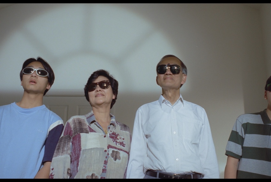 A still from the film Floating Life showing a family of three all looking upwards wearing sunglasses inside. 