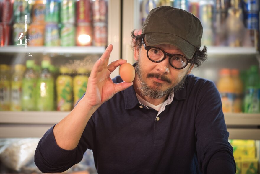 Man with beard, glasses and cap, holding an egg.