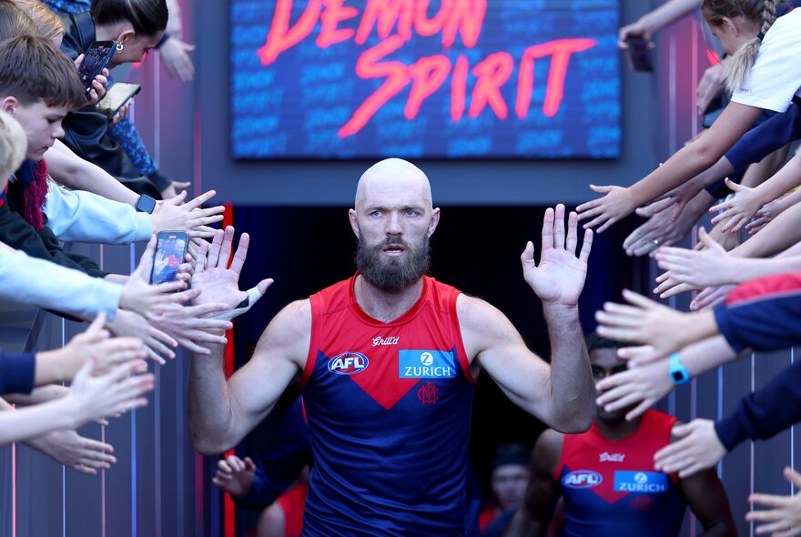 AFL Melbourne player Max Gawn walking onto the football field and past football fans who are holding out their hands to him.