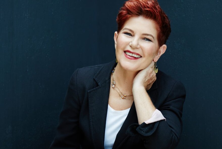 Portrait of award-winning author, Patti Miller, smiling at the camera with a dark blue background.