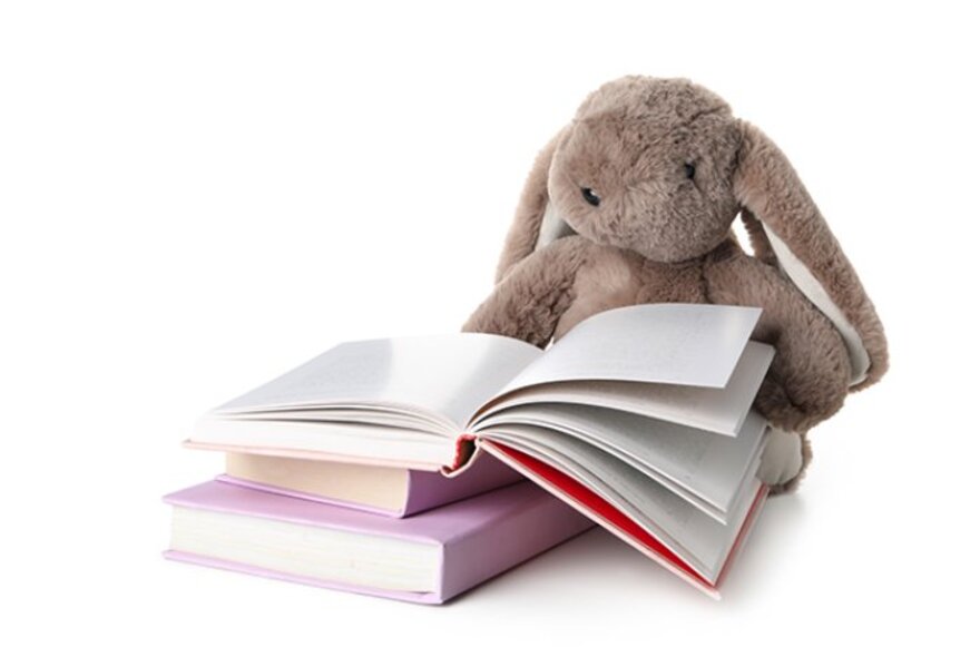 Toy rabbit seated at a pile of books, reading an open book.