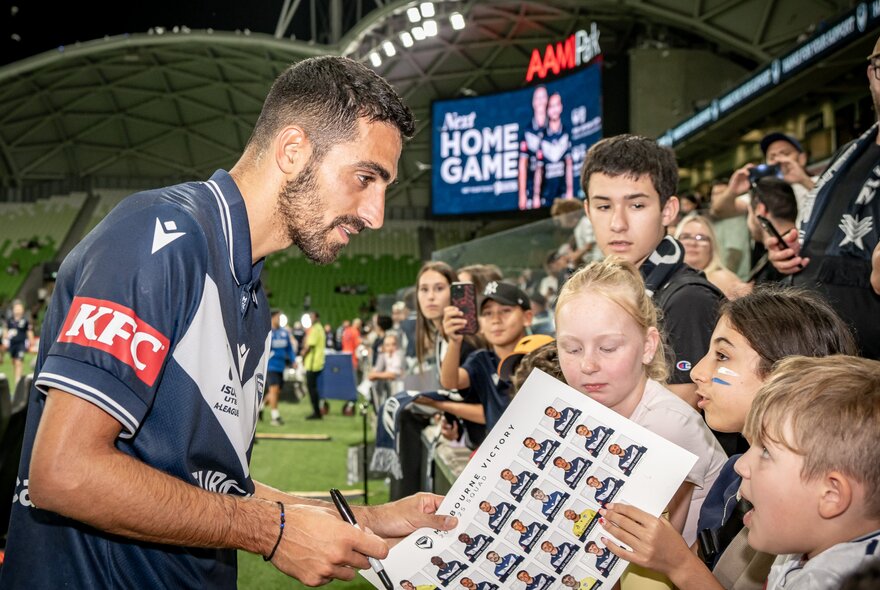 Soccer playing signing a team photo for young fauns at a match.
