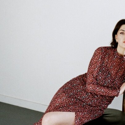 Jazz singer, Elissa Rodger, wearing a glittery, dark red evening dress and leaning on a small leather chair in front of a white wall.