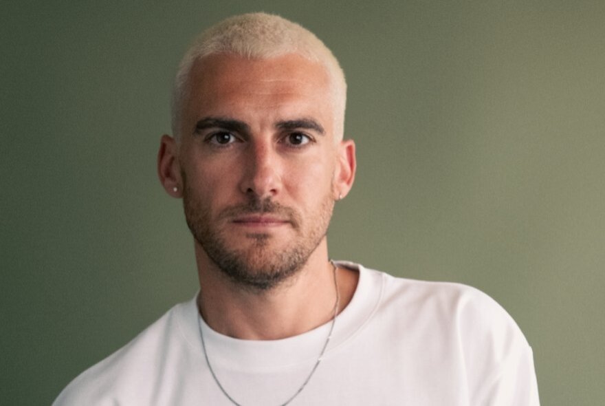 Josh Silver, with beard and silver dyed hair, wearing a white T-shirt.