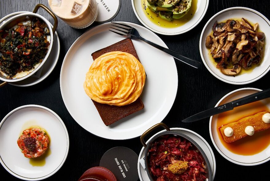 Overhead view of cafe dishes including scrambled eggs swirled on toast, stewed mushrooms and desserts.