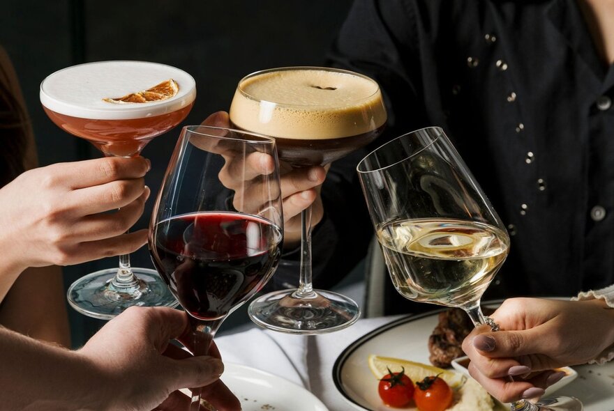Four people raising a toast with a selection of drinks, including red wine, white wine, an espresso martini, and a cocktail.