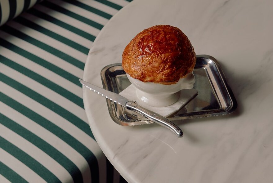 A curry and roti pot pie served on a tray with a knife alongside.