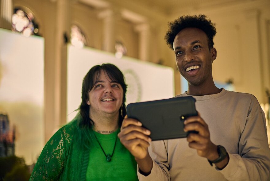 Two smiling museum patrons using a HistoPad, an augmented reality device, to learn more about Notre Dame. 