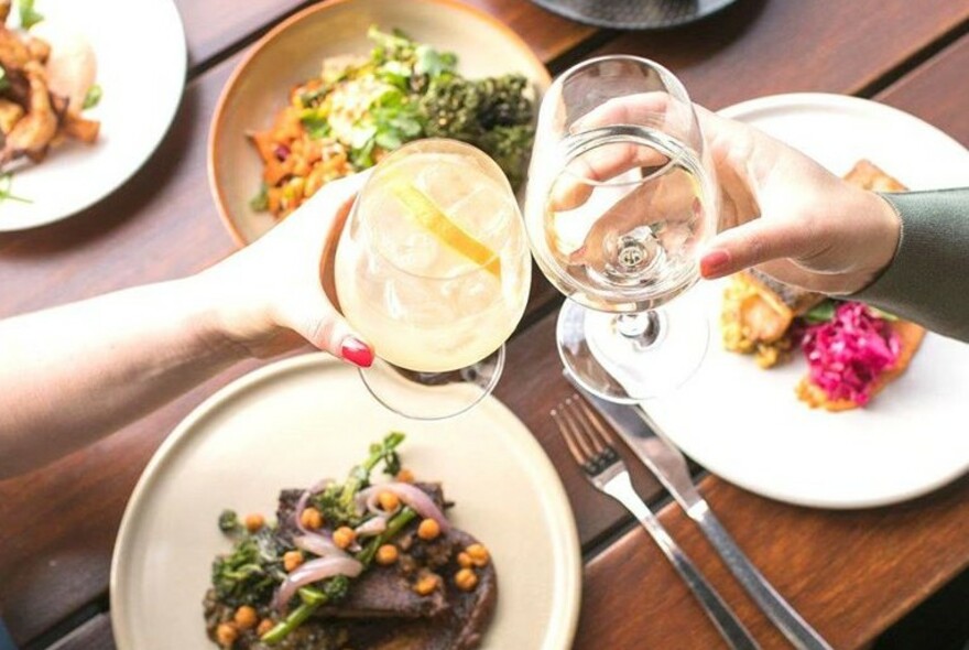 People clinking glasses over plates of food. 