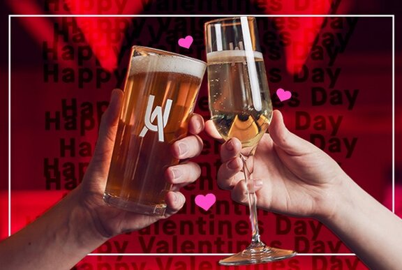 Two people's hands, one holding a schooner of beer the other holding a glass of sparkling wine; red background with pink hearts.