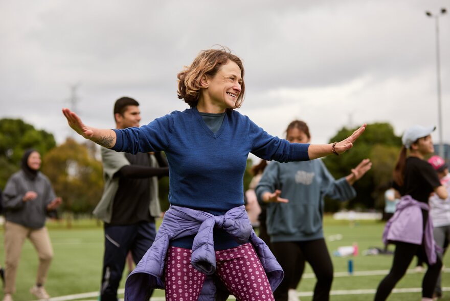 A group of people participating in an outdoor movement or wellness session on a grassy field.