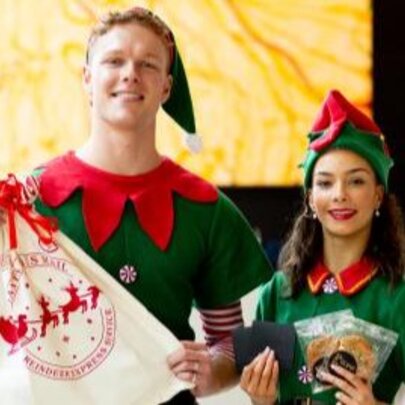 Two people wearing Christmas elf outfits holding gifts.