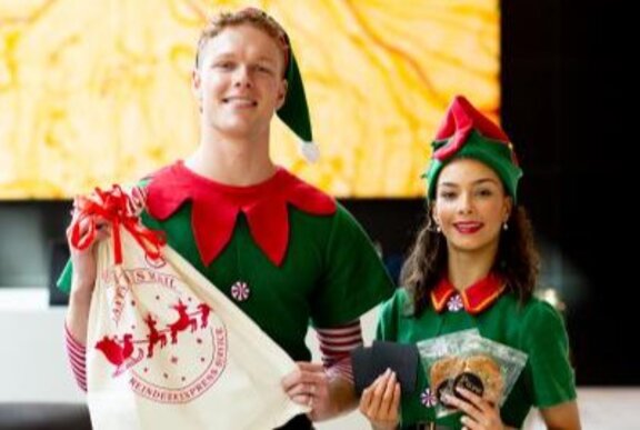 Two people wearing Christmas elf outfits holding gifts.
