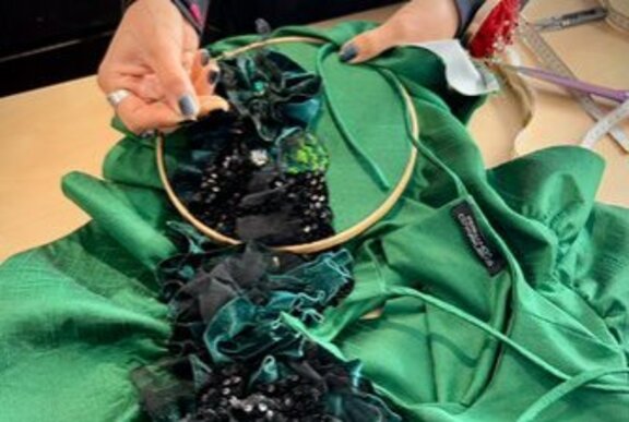 Jewelled embroidery being added to green fabric using an embroidery hoop.