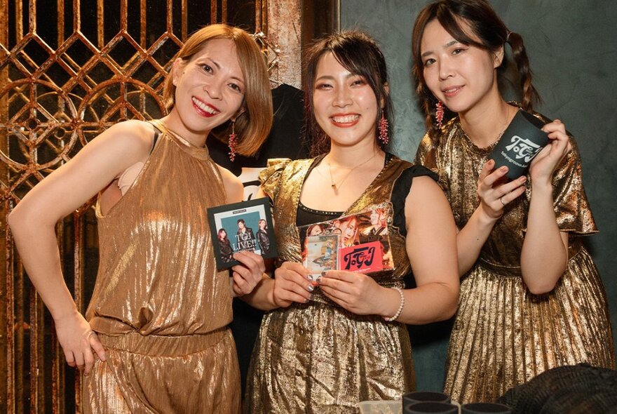 The three members of Tokyo Groove Jyoshi smiling and holding up band merchandise.