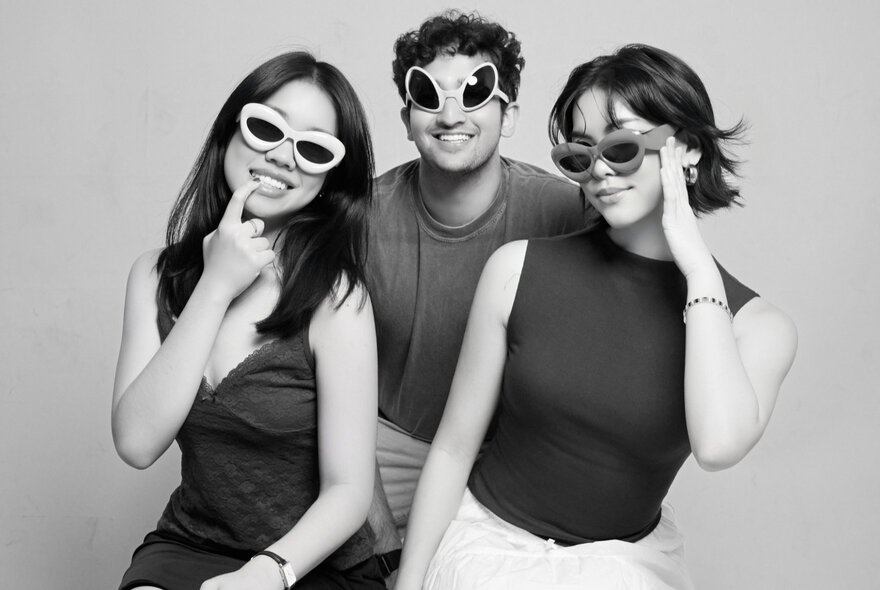 Three friends posing for a photo all wearing oversize sunglasses; black and white.
