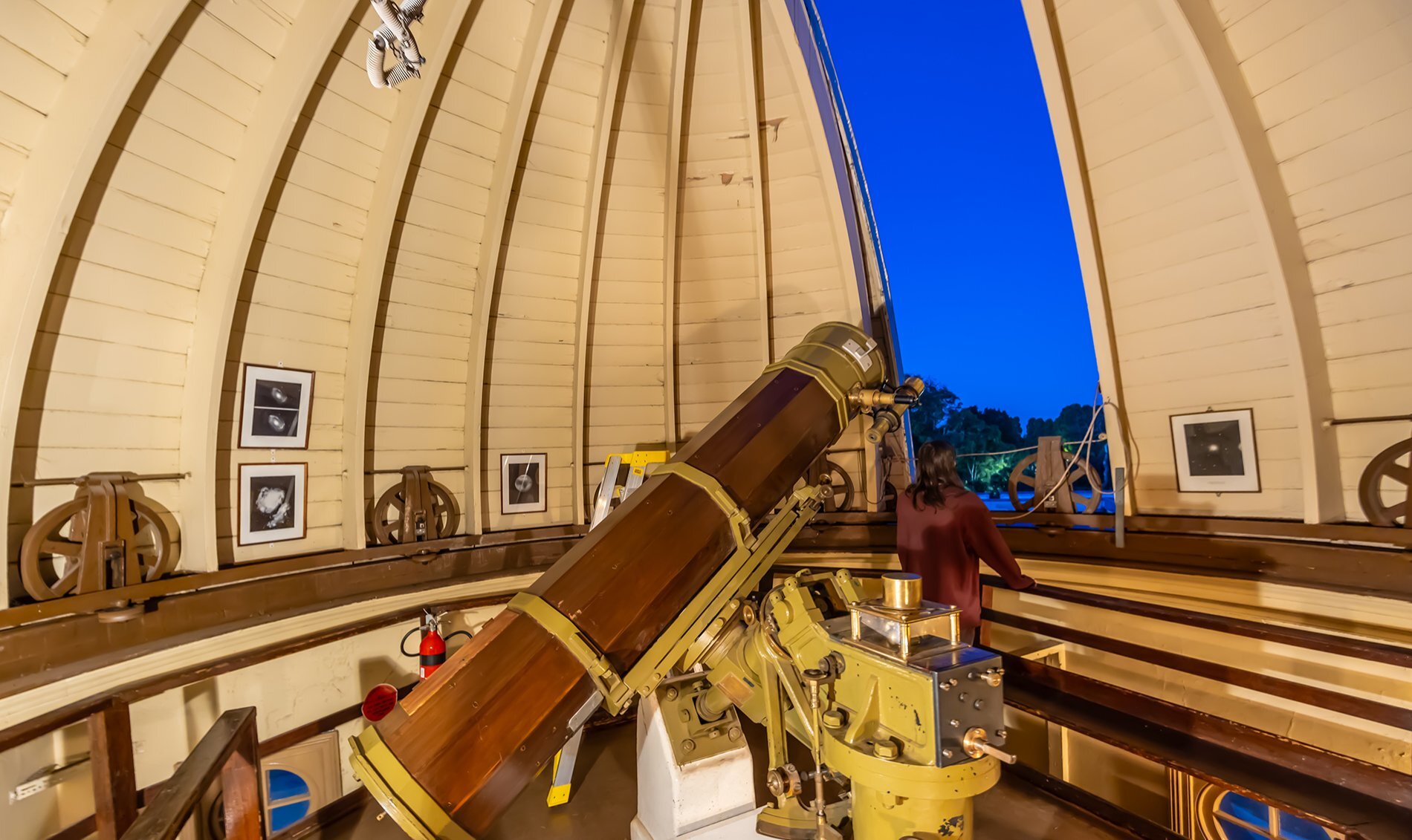 A giant telescope in a room with a domed roof, and a woman looking out an opening into a dark blue sky.