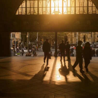 Dark interior of Flinders Street Railway Station entry with light filtering through art nouveau stained glass window onto silhouetted figures.