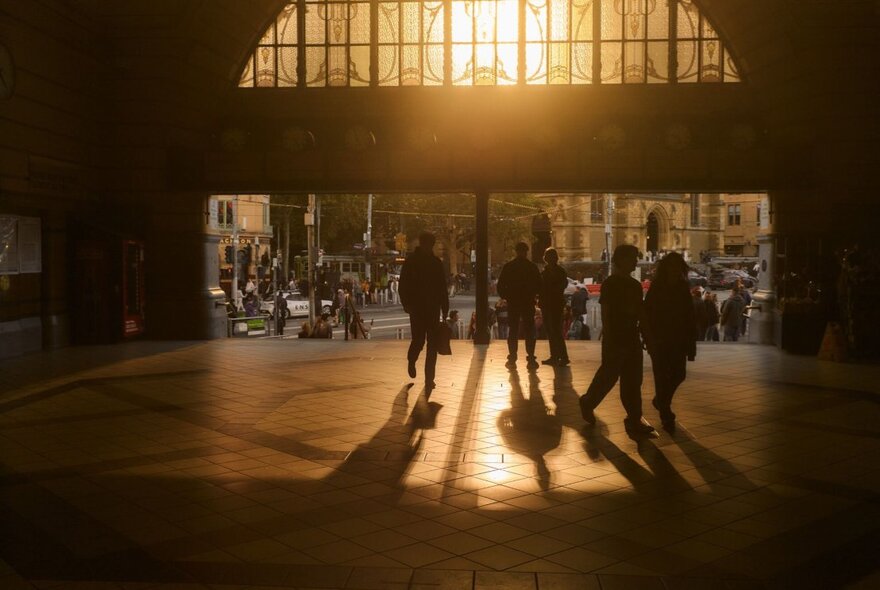 Dark interior of Flinders Street Railway Station entry with light filtering through art nouveau stained glass window onto silhouetted figures.