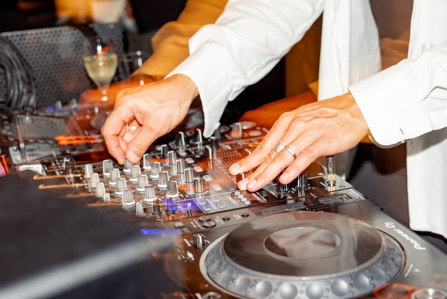Hands working a mixing desk, wine in the background. 