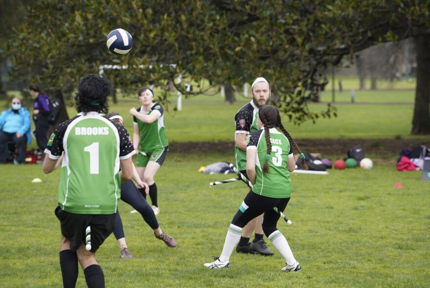 Several people playing an outdoor sport, quadball (formerly Quidditch), in a green open park.