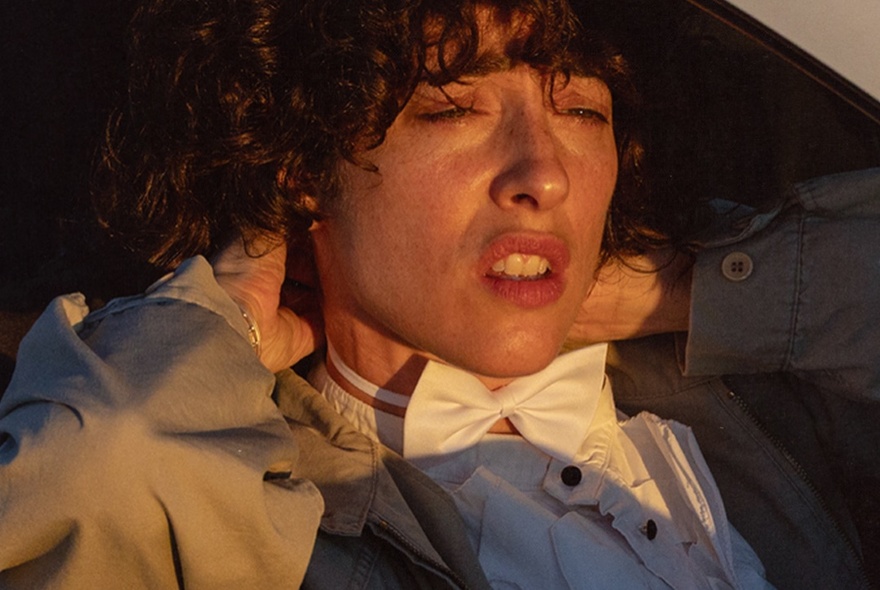 Comedian Hannah Camilleri wearing a white bowtie, looking pained. 