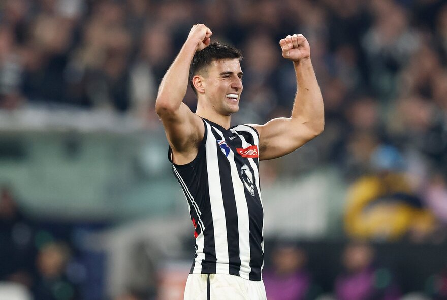 A Collingwood Magpies AFL player with both fists in the air in celebration during a game.