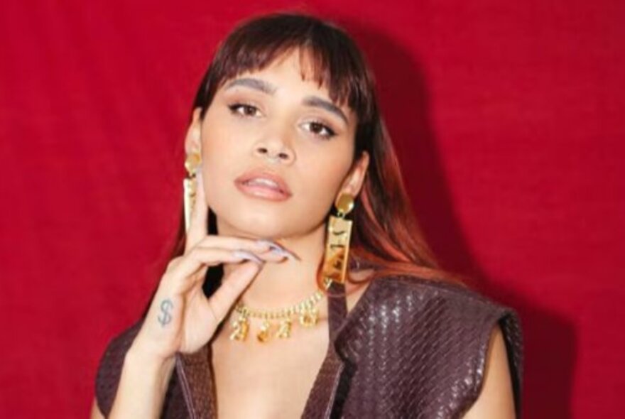 Performer Sky Thomas (Soju Gang), her chin on her hand, with long hair, wearing gold jewellery.