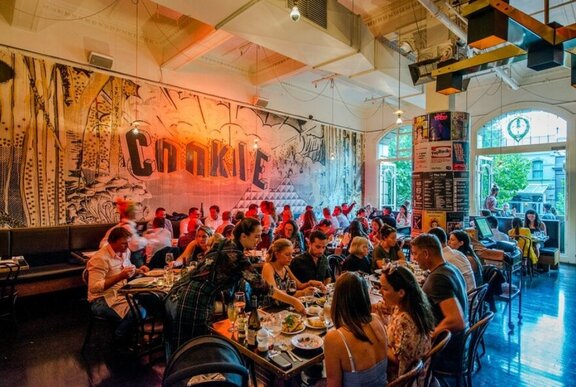 Restaurant patrons seated at tables in a busy restaurant with mural artwork on the walls.