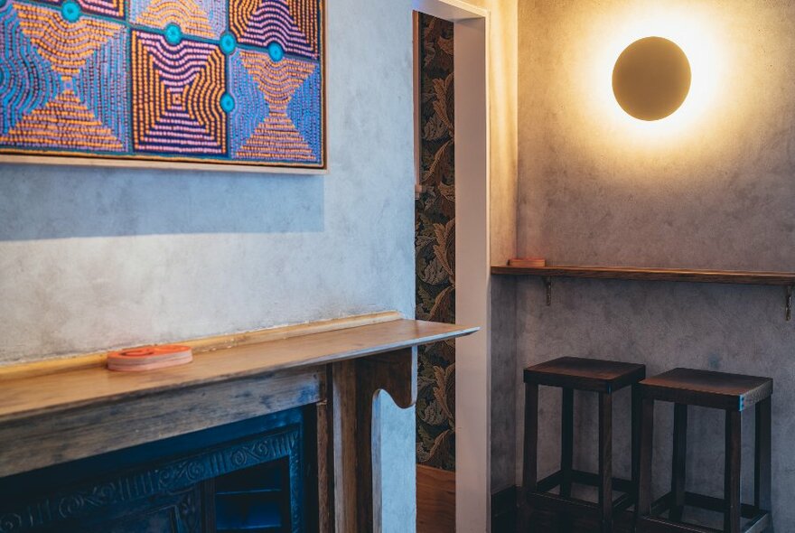 A bar interior with stools, wall lighting and artworks.