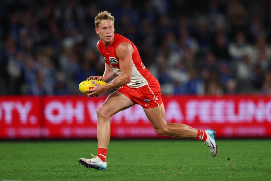 Sydney Swans AFL football player running on the field holding the ball during a match.