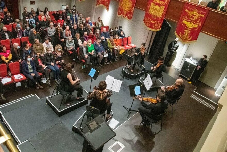 Stage with six musicians seen from above, red banners to right, audience to right.